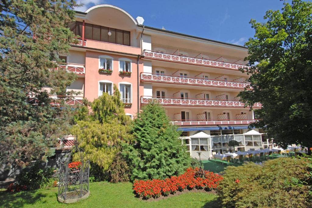 ein großes rosafarbenes Gebäude mit einem Garten davor in der Unterkunft Dermuth Hotels – Hotel Sonnengrund in Pörtschach am Wörthersee