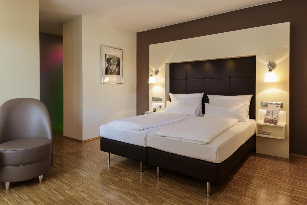 a bedroom with a large bed and a chair at Hotel Santo in Cologne