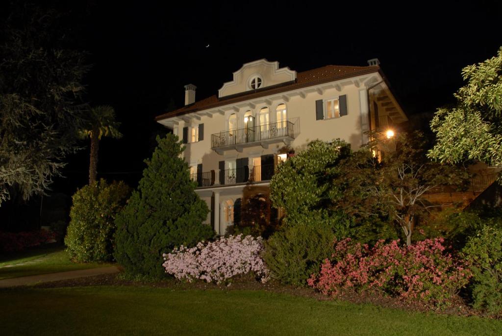una grande casa bianca di notte con alberi e cespugli di B&B Le Camelie a Domodossola