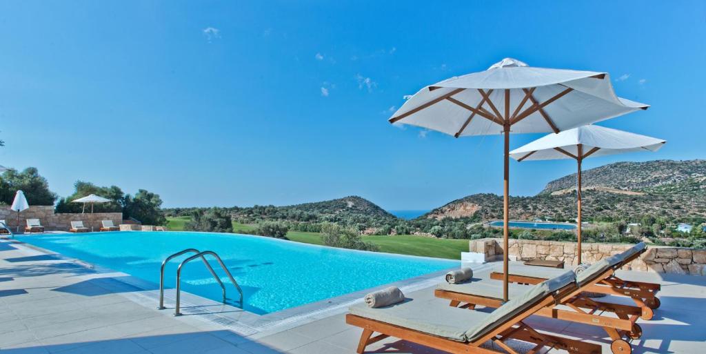 a swimming pool with chairs and umbrellas next to a swimming pool at Crete Golf Club Hotel in Hersonissos