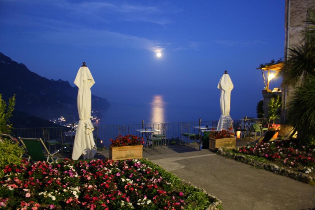 a patio with tables and white umbrellas at night at Hotel Parsifal - Antico Convento del 1288 in Ravello