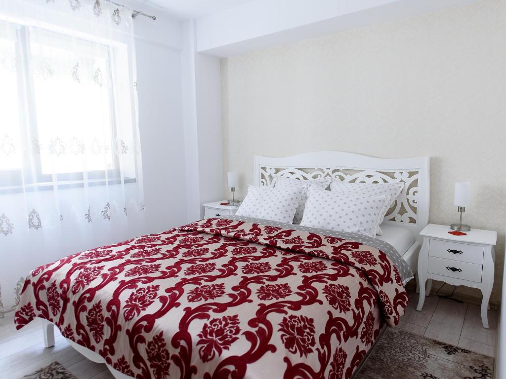 a white bedroom with a red and white bed and a window at Carla's apartment, airport & train station shuttle in Iaşi