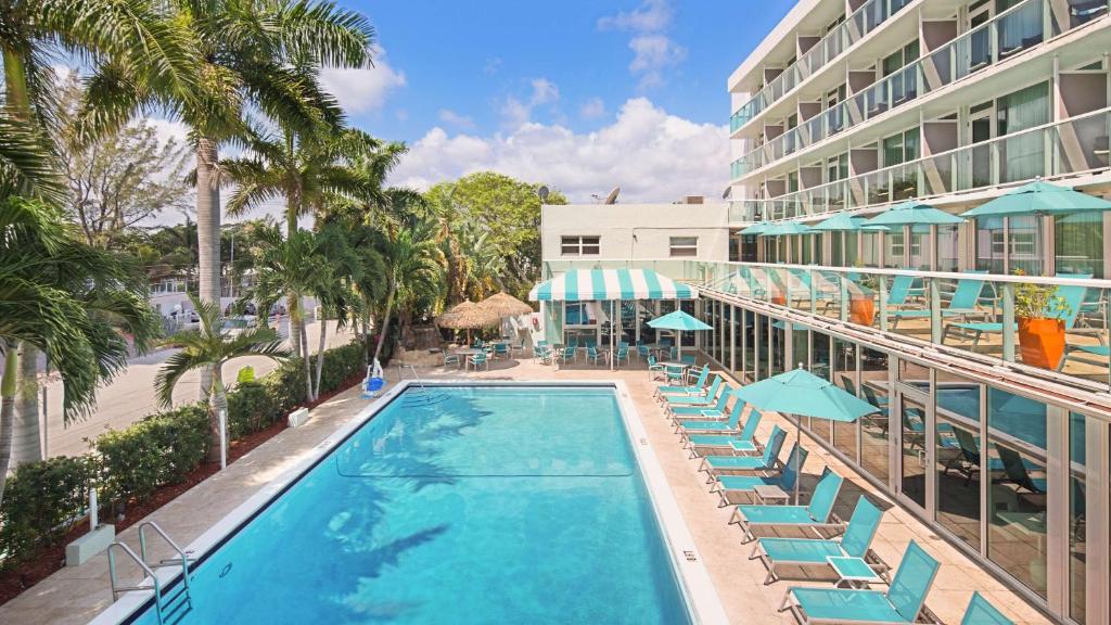 a pool with chairs and umbrellas next to a hotel at Best Western Plus Oceanside Inn in Fort Lauderdale