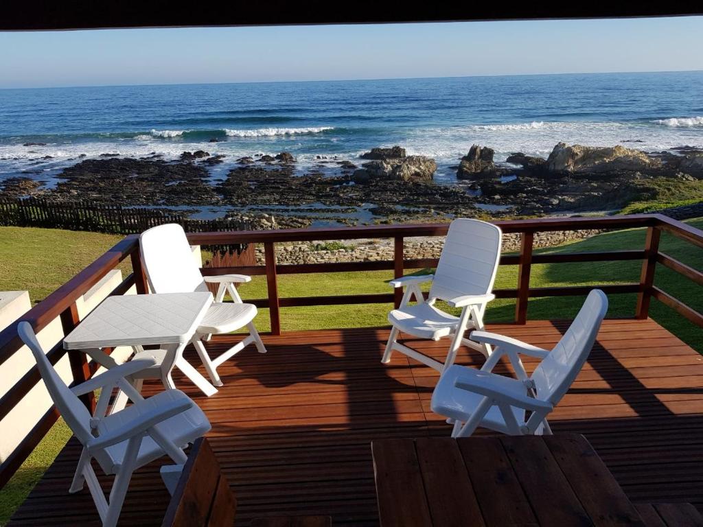 trzy krzesła i stół na tarasie z oceanem w obiekcie Sea Notes Guest House w mieście Port Elizabeth