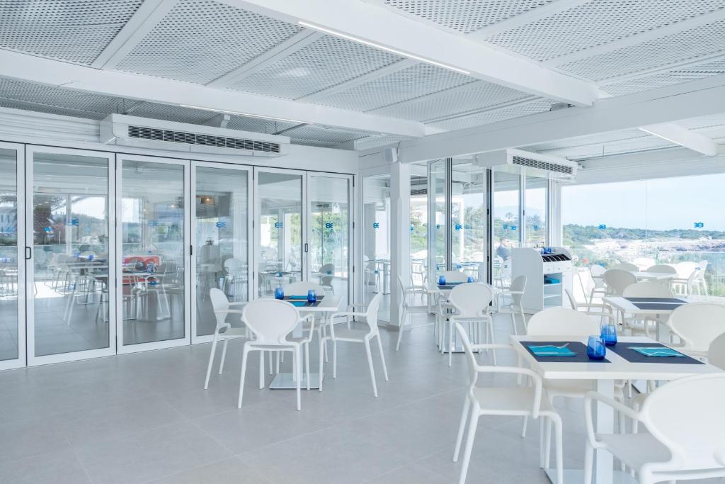 a white room with white chairs and tables and windows at FERGUS Style Carema Beach in Cala en Bosc