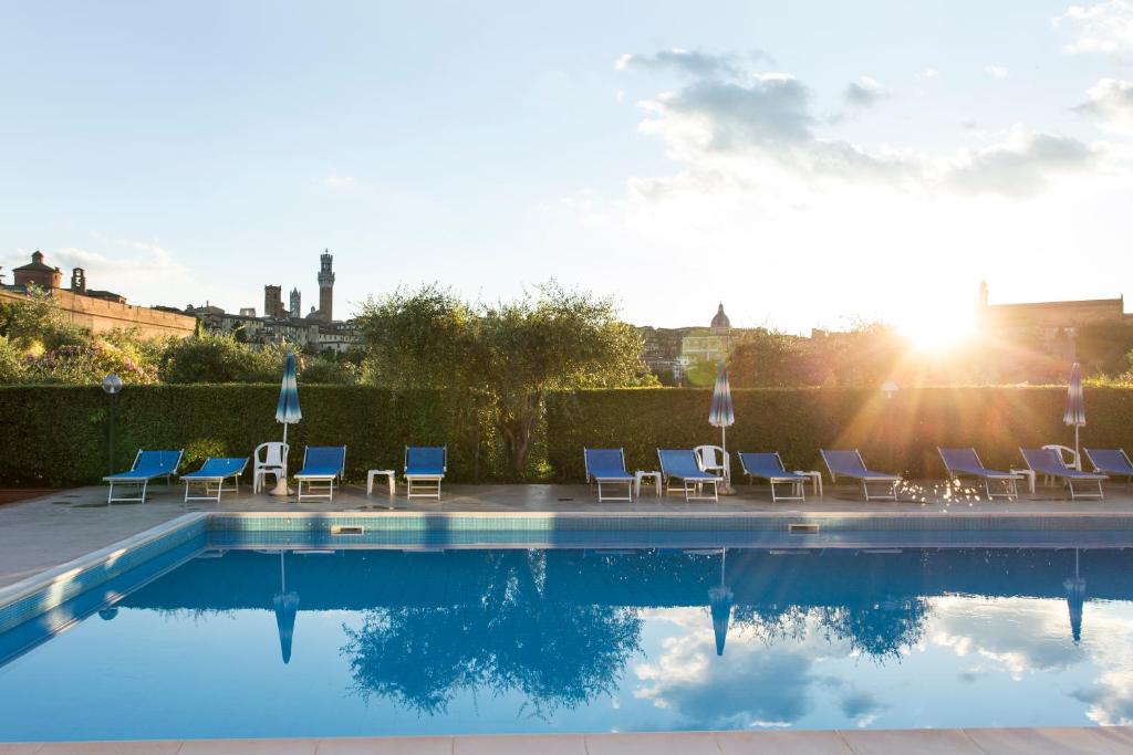 a swimming pool with chairs and the sun setting at Hotel Il Giardino in Siena