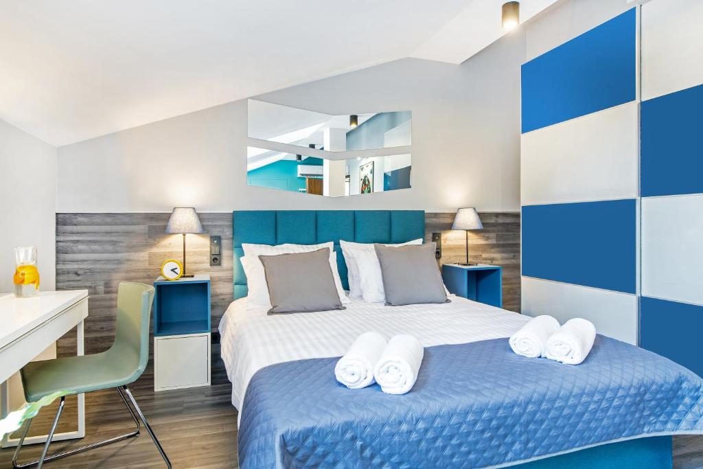 Modern bedroom with teal headboard, white linens, blue quilt and neatly rolled towels.