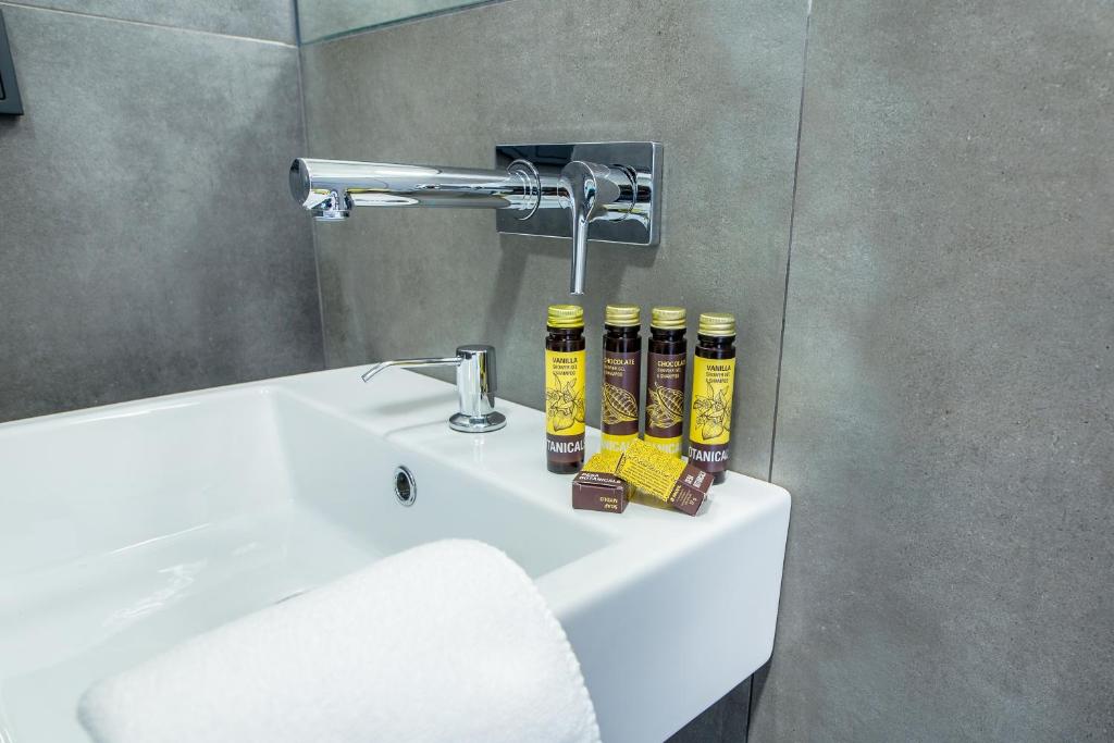 White sink with chrome wall faucet, arranged toiletries and folded hand towel on basin.