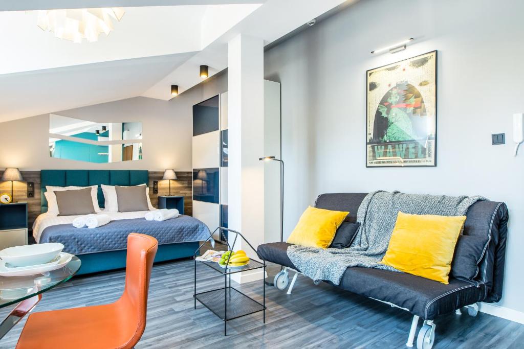 Bright studio with double bed, teal headboard, mirrored wall, gray sofa and yellow cushions.