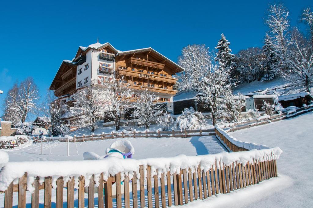 uma criança brincando na neve em frente a uma casa em Hotel Babymio em Kirchdorf in Tirol