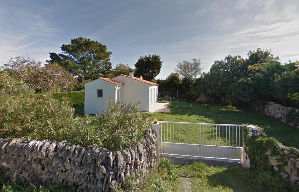 a small white house on a hill next to a stone wall at Location Saint Pierre d'Oléron in La Cotinière