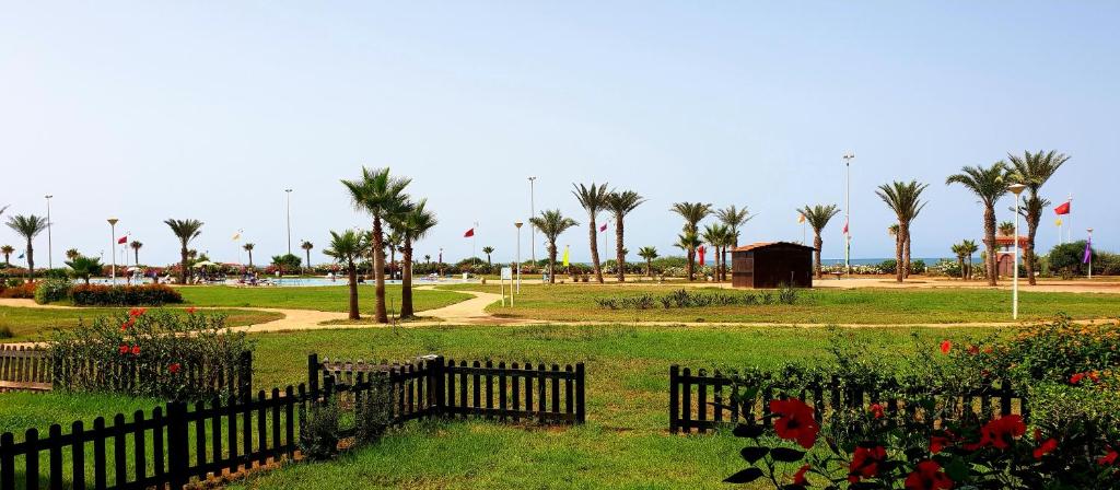 a park with palm trees and a fence and flowers at Perle Orientale Saidia Appart Rénové vue sur jardin et sur mer in Saïdia