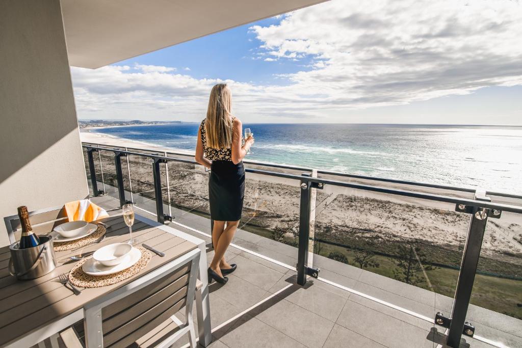 Una mujer parada en un balcón con vistas al océano en Iconic Kirra Beach Resort, en Gold Coast