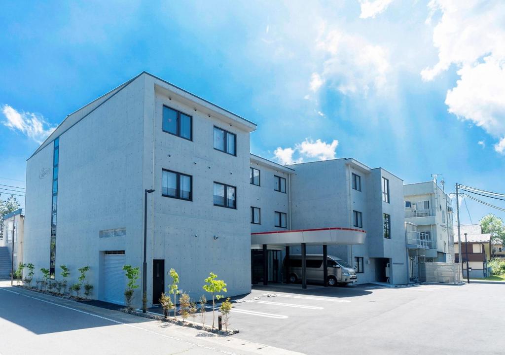 un bâtiment blanc avec une camionnette garée dans un parking dans l'établissement Hotel Rosso Karuizawa, à Karuizawa
