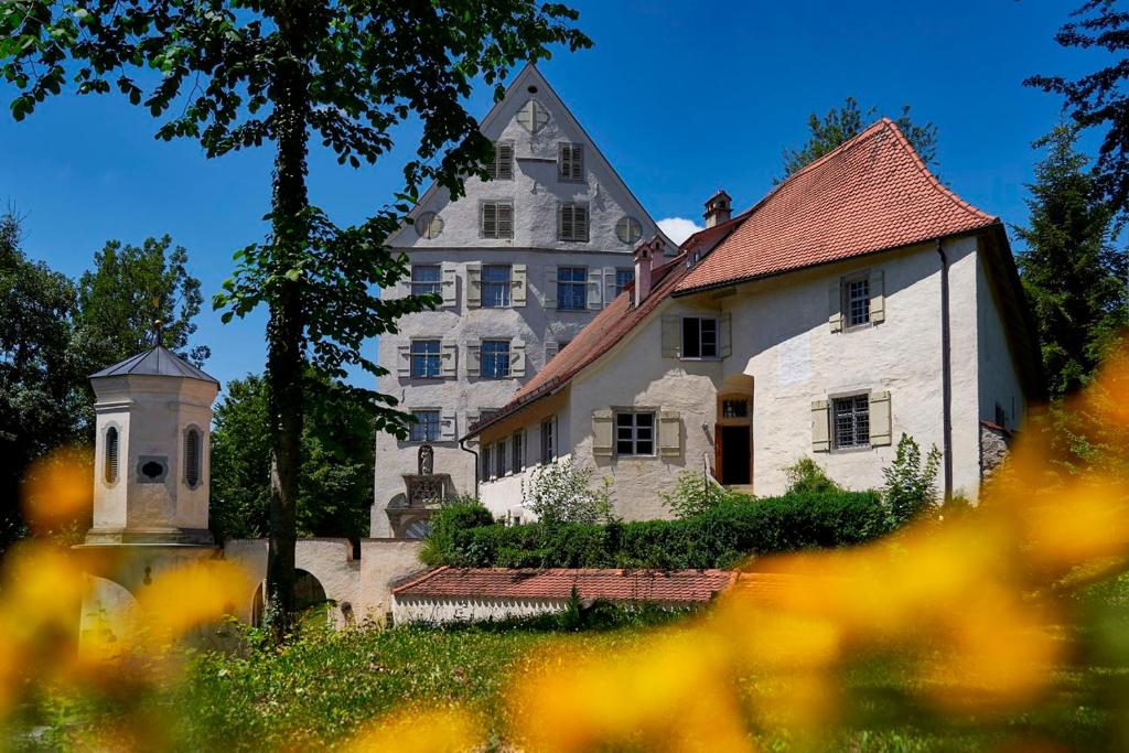 ein großes weißes Haus mit einem Baum und Blumen in der Unterkunft Ferienwohnungen Kommende und Ballei in Achberg