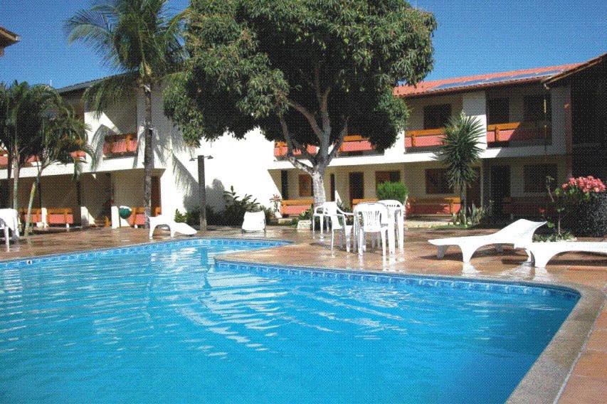una gran piscina con sillas blancas y un edificio en Coroa Bella Praia Hotel, en Coroa Vermelha