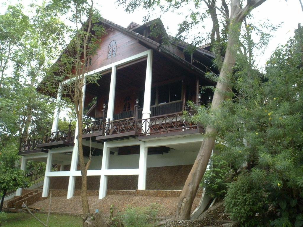 a house with a wrap around porch in the woods at Ratmanee House in Kanchanaburi City
