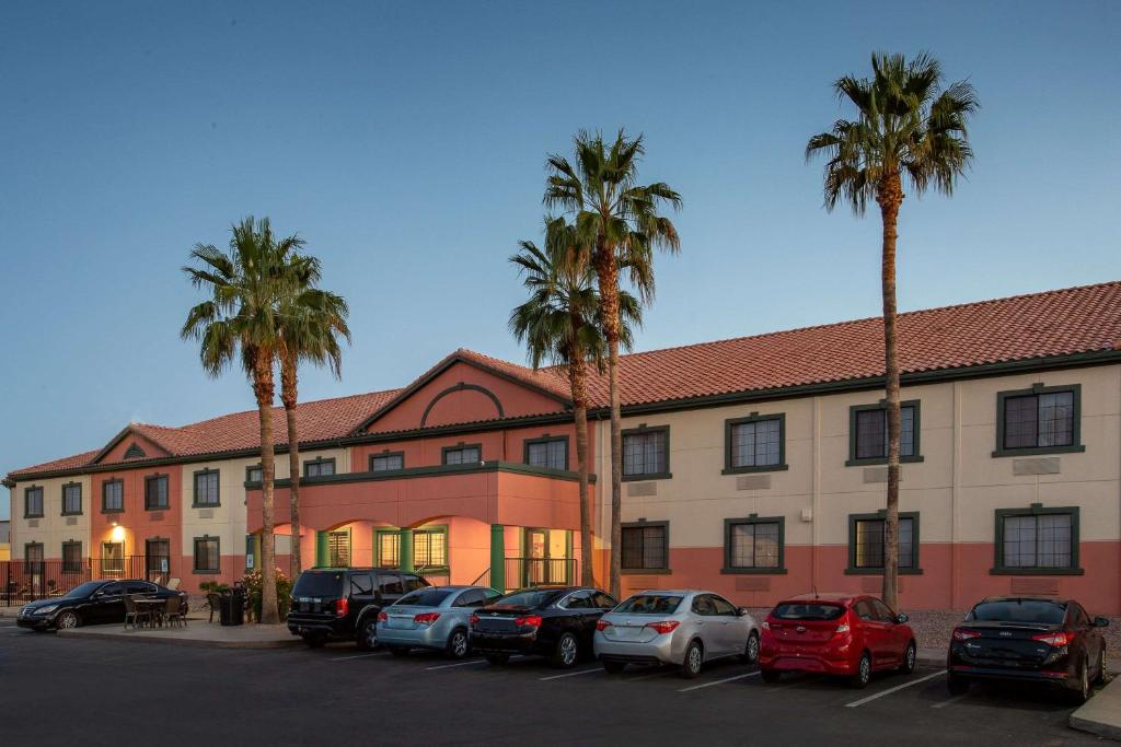 un bâtiment avec des voitures garées dans un parking avec des palmiers dans l'établissement Baymont by Wyndham Phoenix I-10 near 51st Ave, à Phoenix