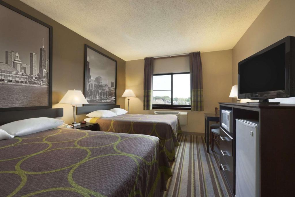 a hotel room with two beds and a flat screen tv at Super 8 by Wyndham Bridgeview/Chicago Area in Bridgeview