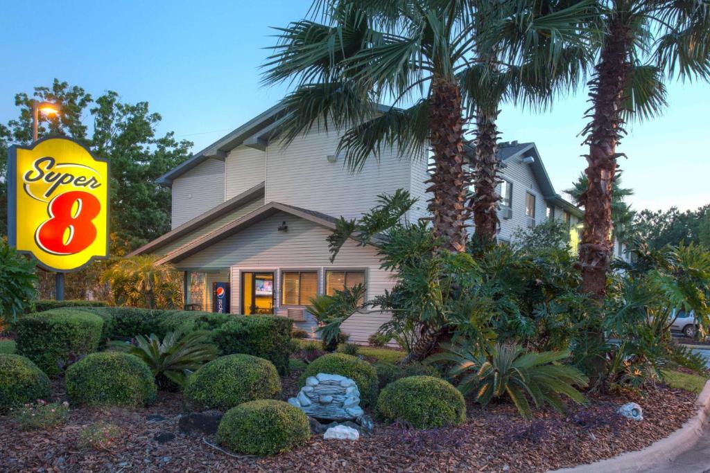 a sign in front of a house with trees and bushes at Super 8 by Wyndham Gainesville in Gainesville