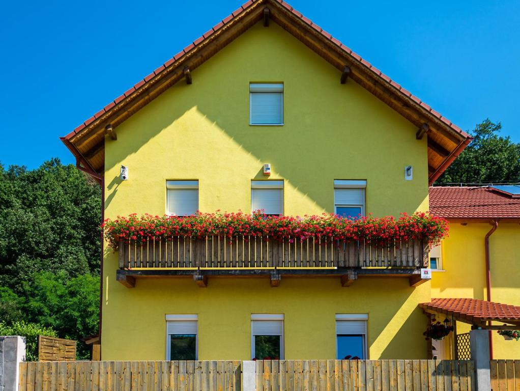a yellow house with a balcony with flowers on it at Bakterház Vendégház in Nagyvisnyó