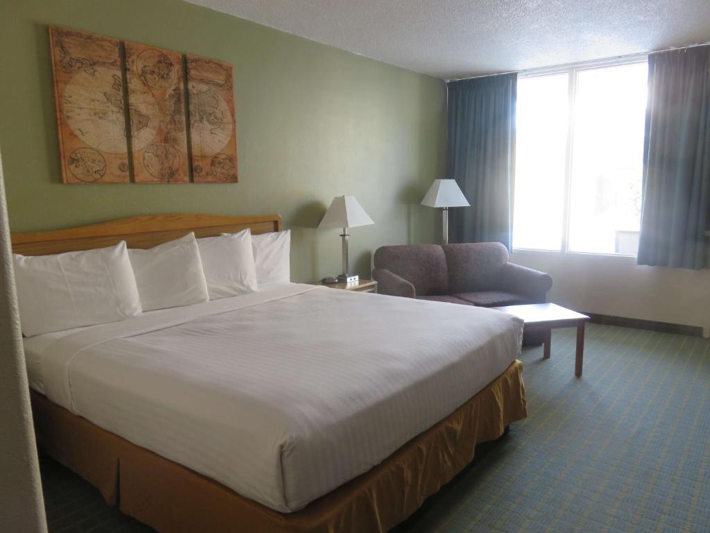 Baymont by Wyndham Fargo في فارغو: غرفة فندقية بسرير كبير وكرسي