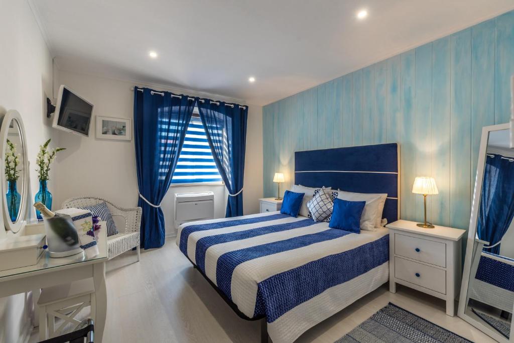 Un dormitorio con una cama azul y blanca y una ventana. en Suites @ Portarade, en Ferragudo