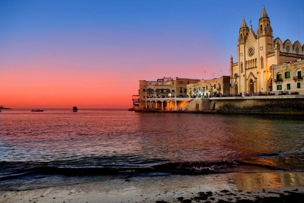 a building next to the water at sunset at Modern 2BR Sliema Apartment in Sliema
