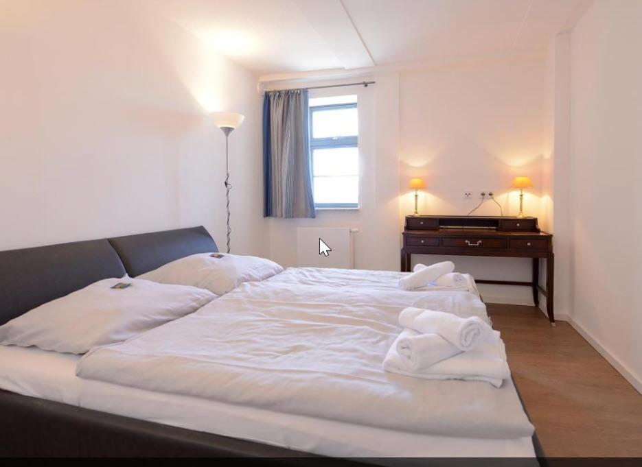 維斯馬的住宿－Appartment im Ohlerich Speicher in Wismar mit Stadt -und Meerblick，一间卧室配有一张带白色床单的床和一张书桌。