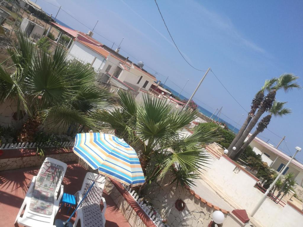 eine Terrasse mit einem Sonnenschirm, Palmen und dem Meer in der Unterkunft Casa Vacanze Villa Giacetta in Santa Maria Del Focallo