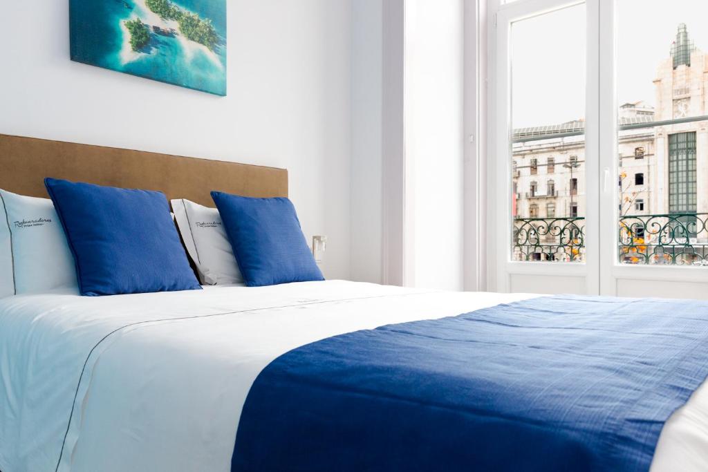 a bedroom with a blue and white bed with a window at Inn-Chiado Restauradores Prime Suites in Lisbon