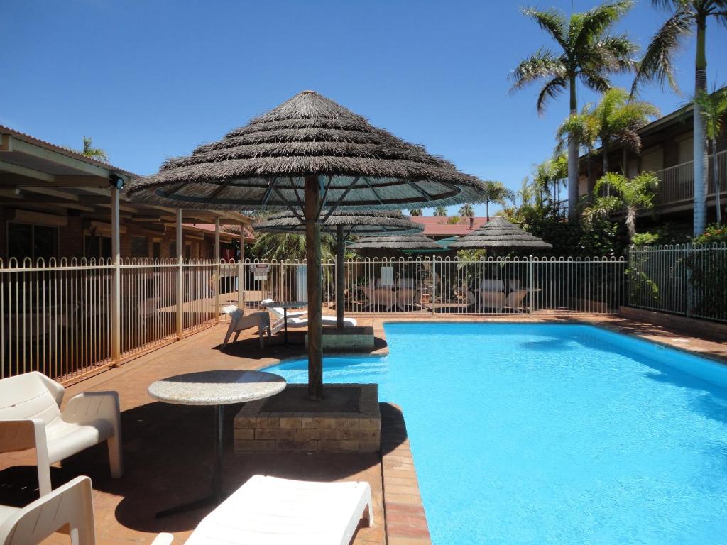 a swimming pool with an umbrella and a table and chairs at The Lodge Motel in South Hedland