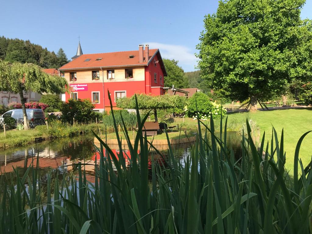uma casa vermelha com um lago em frente em Auberge Restaurant La Roseraie em Grandrupt