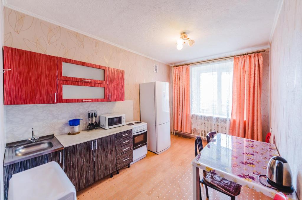 a kitchen with red cabinets and a table and a refrigerator at Dekabrist Apartment Shilova 46 in Chita