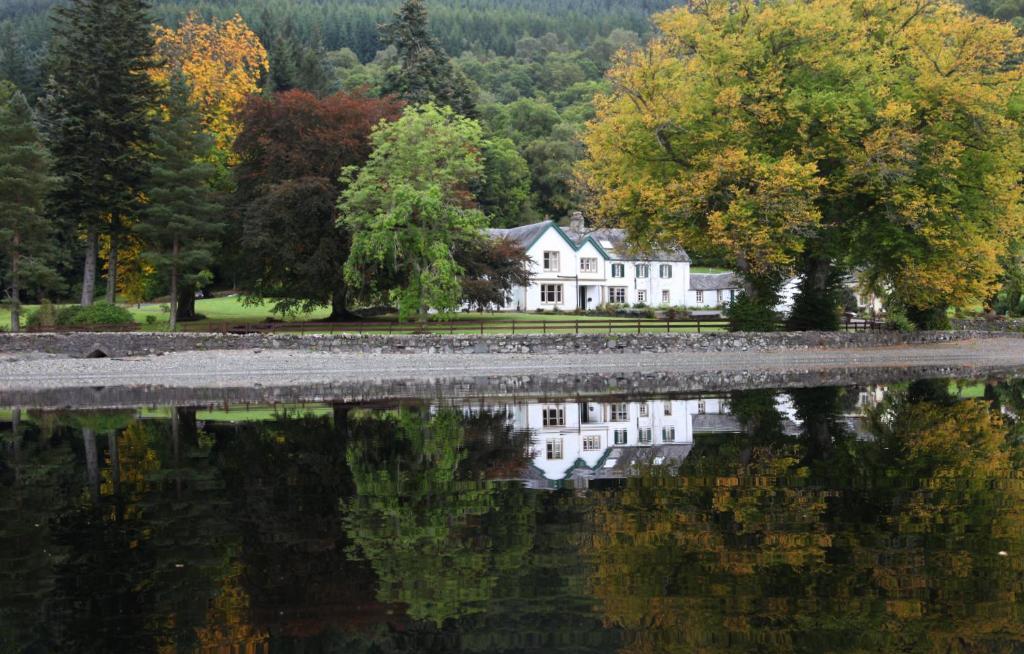 una casa se refleja en el agua de un lago en Altskeith Country House en Aberfoyle