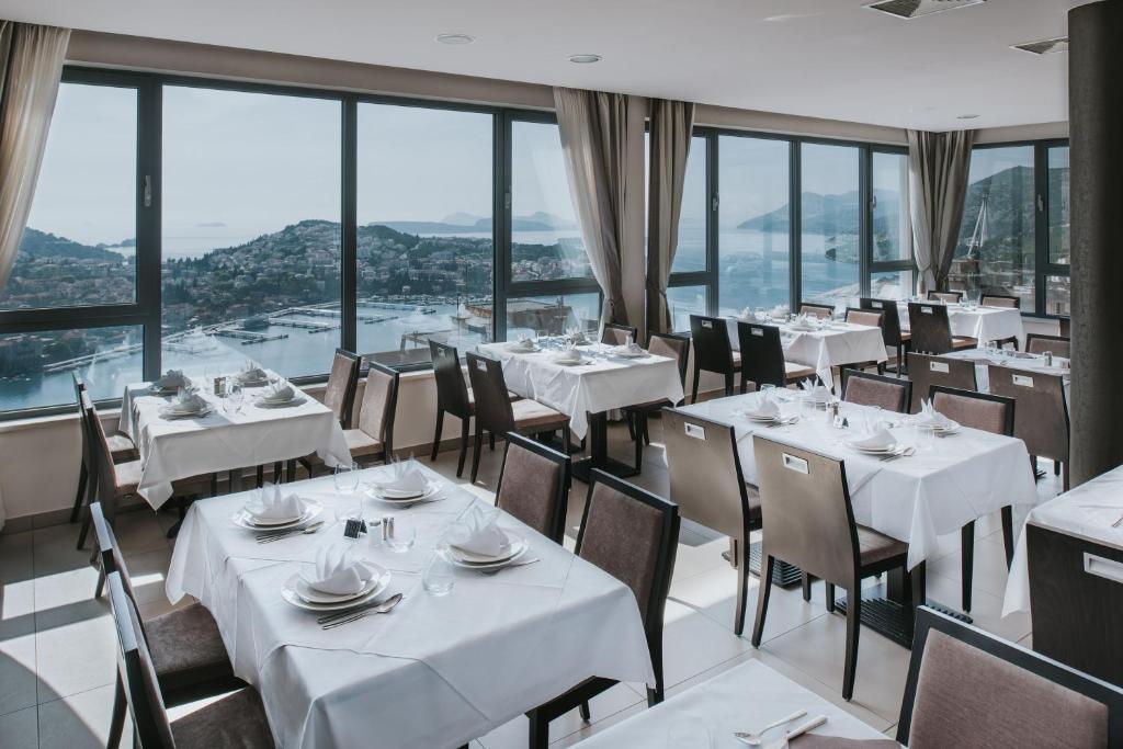 a restaurant with white tables and chairs and windows at Hotel Adria in Dubrovnik