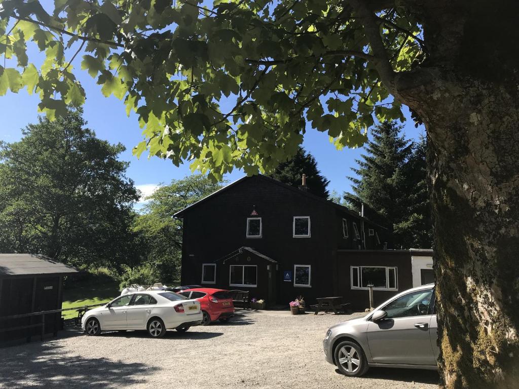 Czarna stodoła z samochodami zaparkowanymi przed nią w obiekcie Glencoe Youth Hostel w mieście Ballachulish