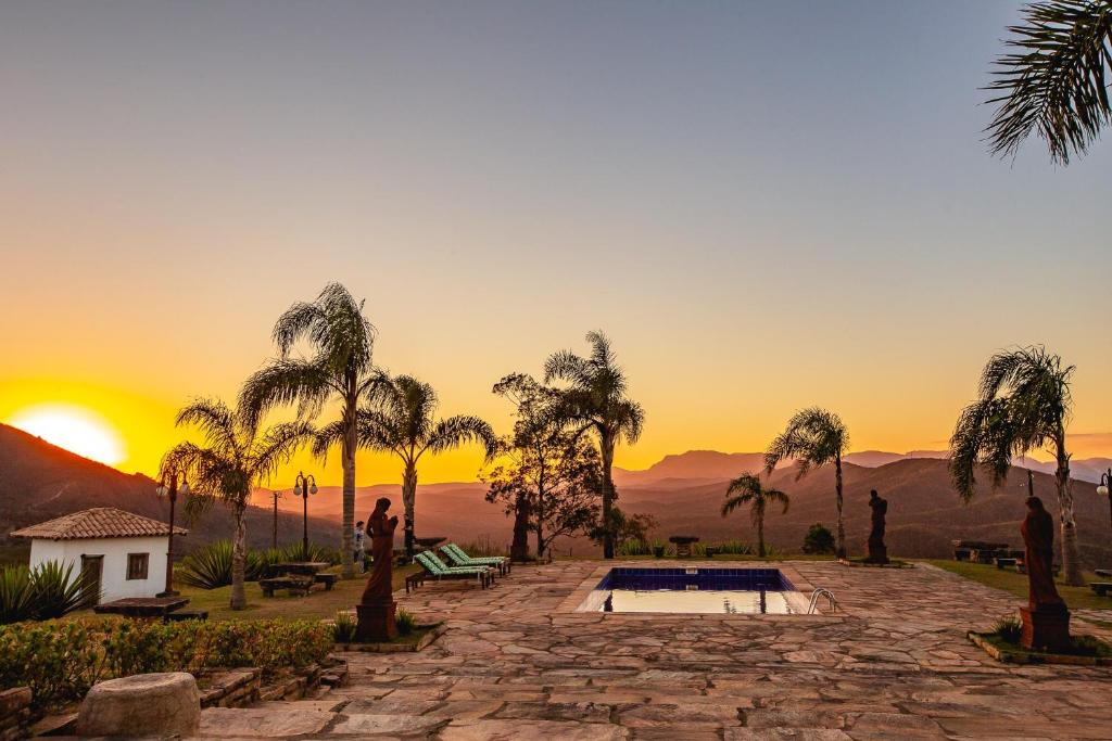 puesta de sol sobre un complejo con palmeras y piscina en Hotel Vila Relicário, en Ouro Preto
