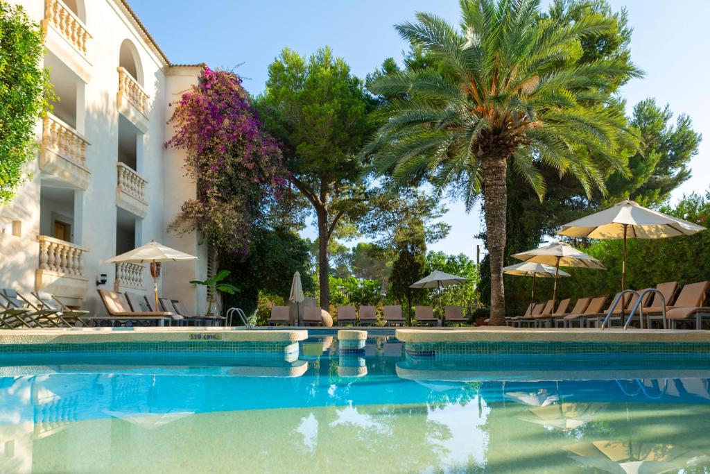 a swimming pool in front of a building with palm trees at Es Baulo Petit Hotel in Can Picafort