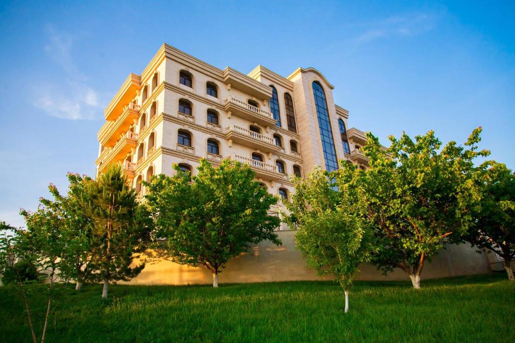 un gran edificio con árboles delante de él en Kainar Hotel en Shymkent