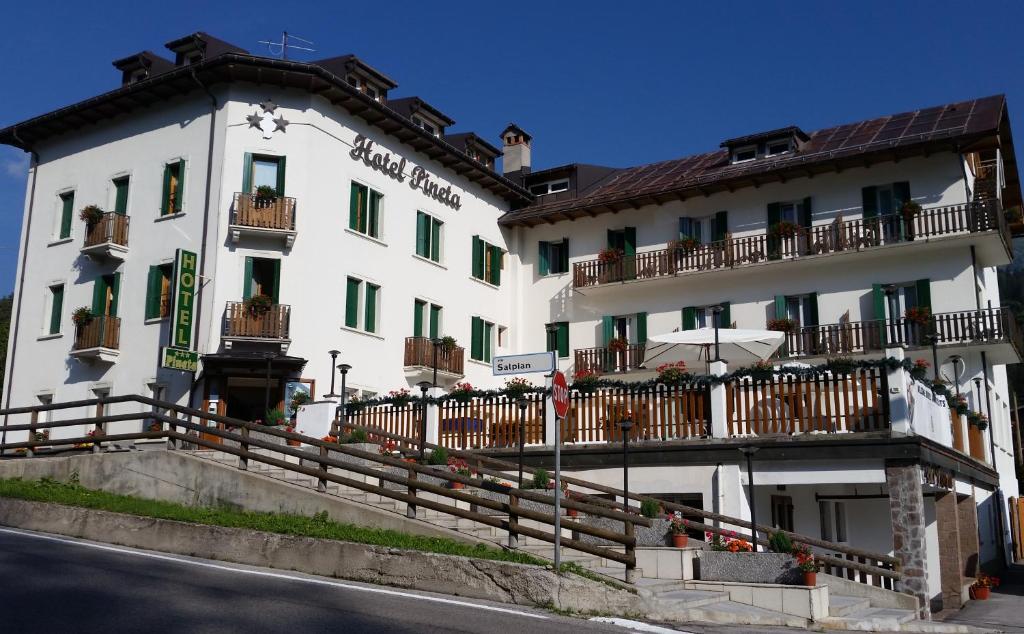 un grand bâtiment blanc avec une clôture devant lui dans l'établissement Hotel Pineta, à Falcade