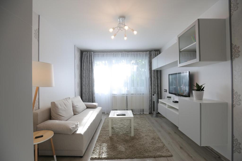 ein weißes Wohnzimmer mit einem Sofa und einem TV in der Unterkunft Modern & Homely Apartment - FREE PARKING - NETFLIX in Kaunas