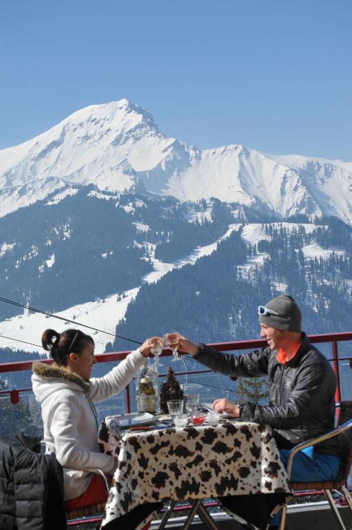 a man and woman sitting at a table in front of a mountain at L'Escale (accès en télécabine) in Châtel