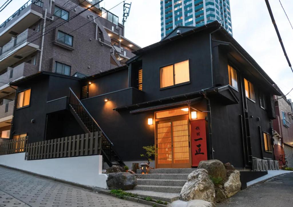 a black house with a red door and some buildings at Ryokan Ichinao in Tokyo