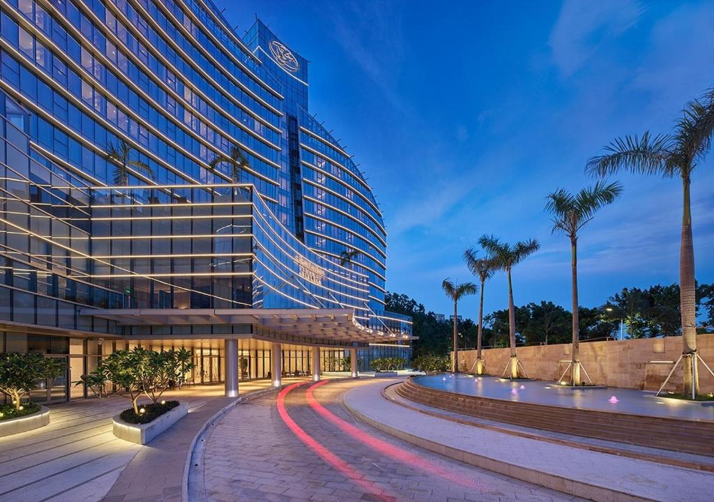 a large building with palm trees in front of a road at Grand Bay Hotel Zhuhai in Zhuhai