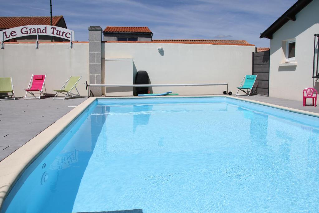 une grande piscine avec des chaises et un bâtiment dans l'établissement Logis Hotel Restaurant Le Grand Turc, à LʼOie