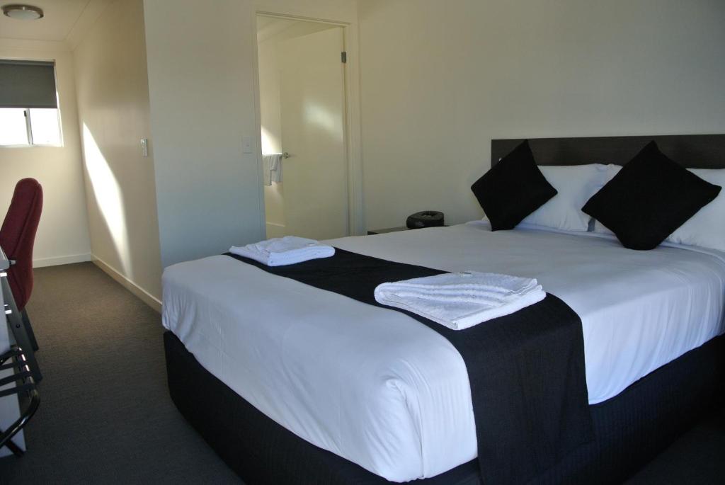 1 dormitorio con 1 cama grande con sábanas blancas y almohadas negras en Dooley's Tavern & Motel Springsure en Springsure