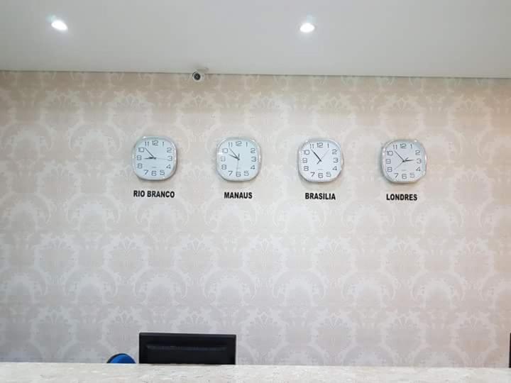 quatre horloges sur un mur avec des fuseaux horaires différents dans l'établissement Hotel Loureiro, à Rio Branco