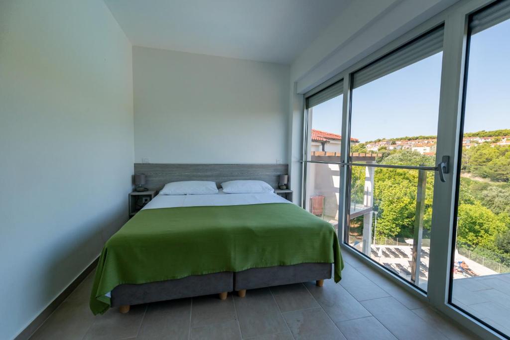 a bedroom with a green bed and large windows at Premantura Resort - Hotel & Restaurant in Premantura