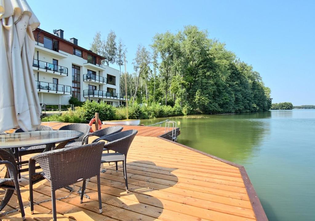 a wooden deck with chairs and tables next to a river at Apartament plażowy Ukiel in Olsztyn